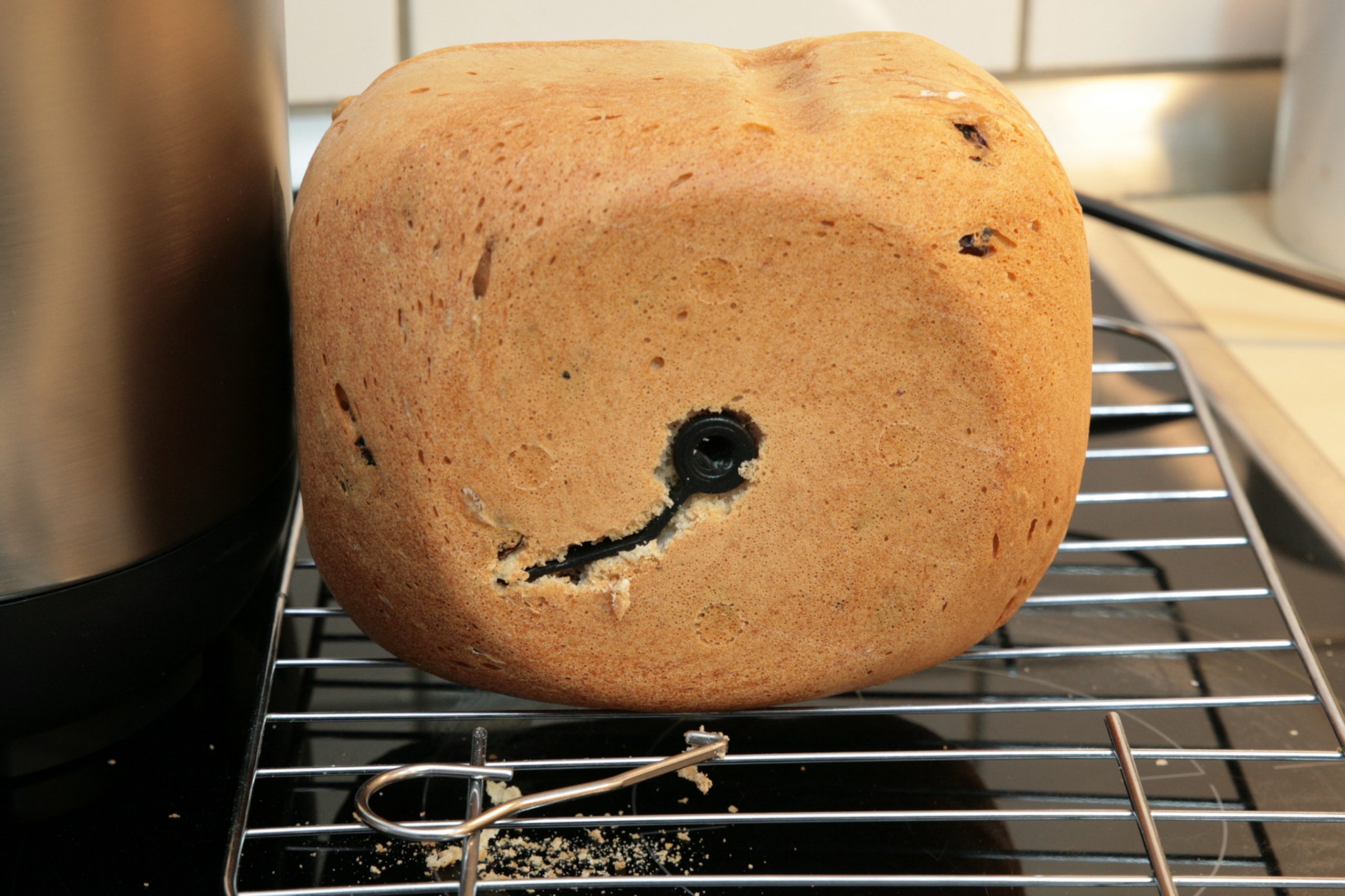 Helles ovales Brot von vorne mit Loch und Riss auf Rost, davor ein Metalhaken