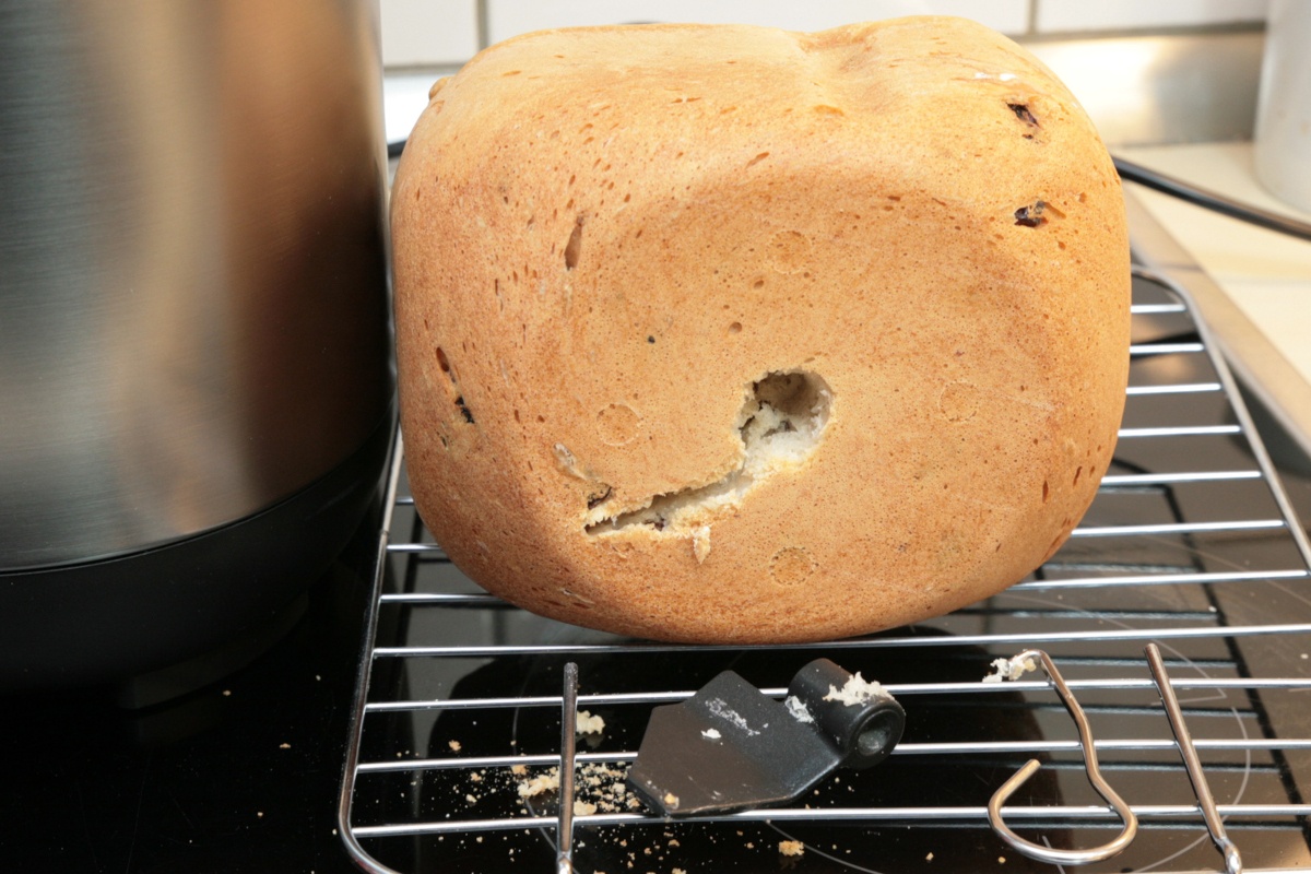 Helles ovales Brot auf Rost mit Riss und Loch, davor liegt Knethaken