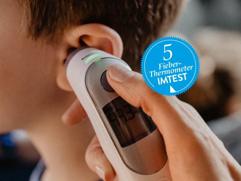 Ein Fieberthermometer wird an das linke Or eines Kindes gehalten.