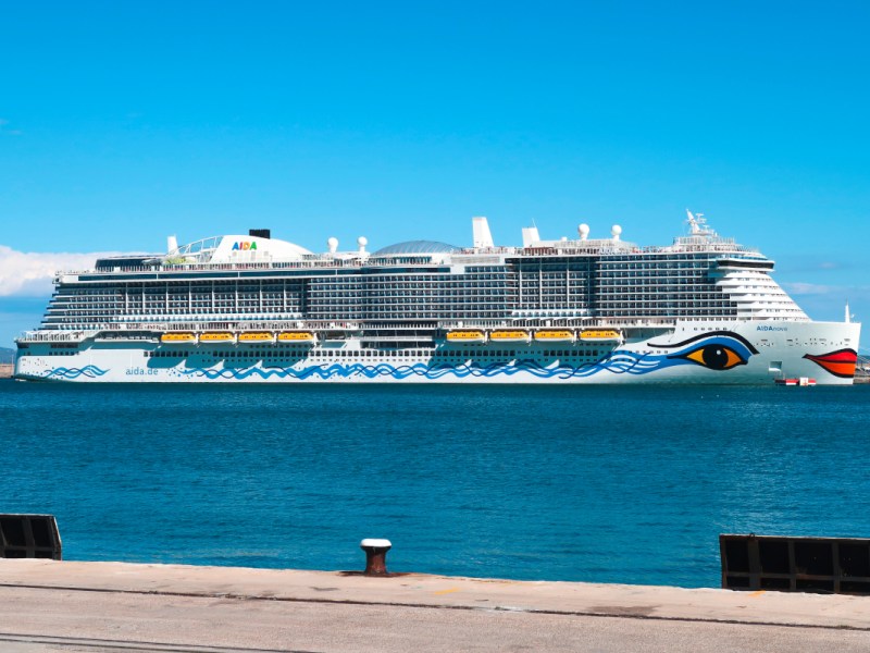 Von Hafenkante Blick auf blaues Wasser mit großem AIDA-Schiff am Horizont