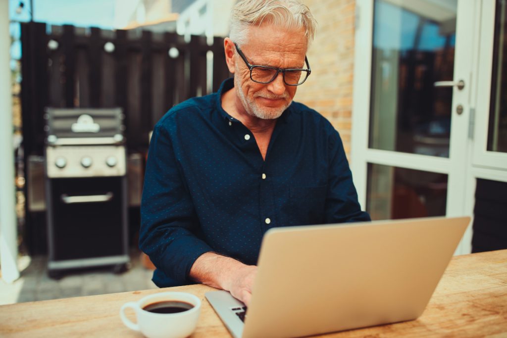 Älterer Mann mit Brille sitzt lächelnd am Notebook