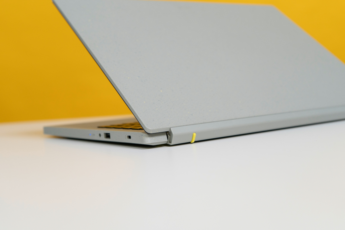 halb zugeklapptes graues Notebook schräg von hinten auf Tisch vor gelber Wand