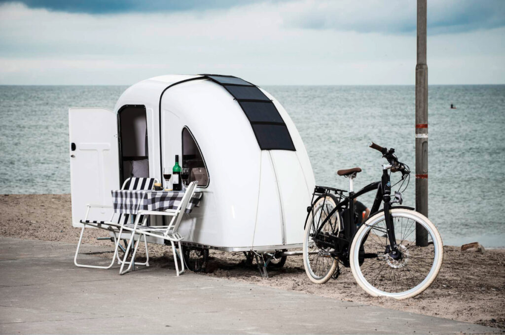 Weißer Anhänger mit offener Tür vor Fahrrad am Strand