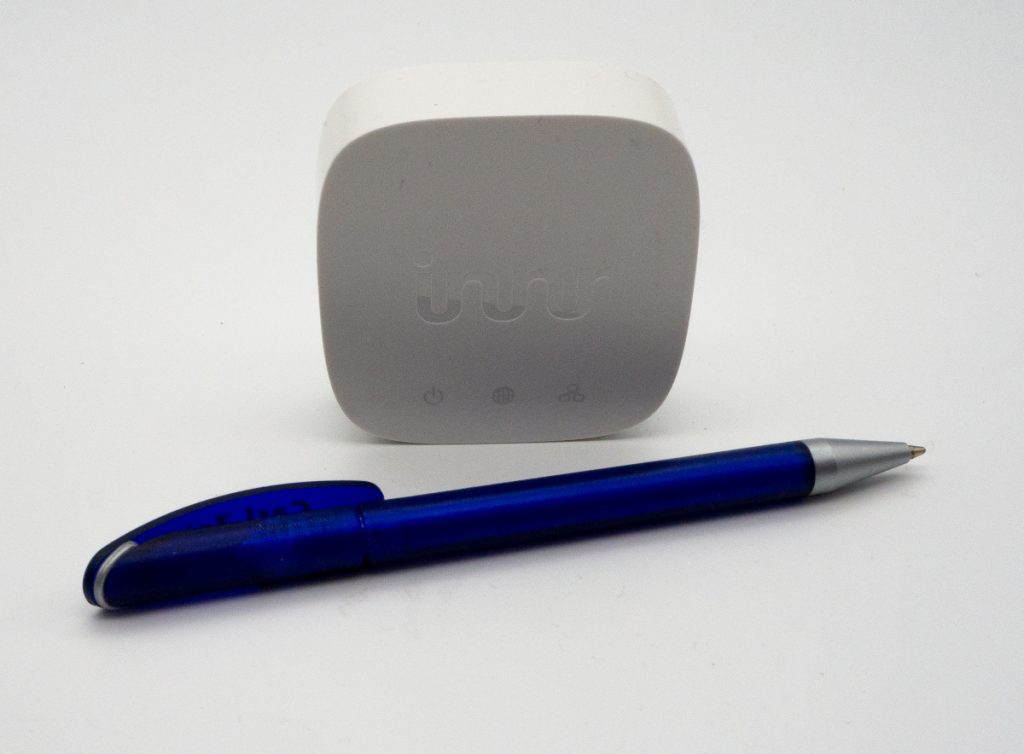 Kleines weißes quadratisches Gerät auf weißem Grund hinter blauem Kugelschreiber, der länger als das Gerät ist