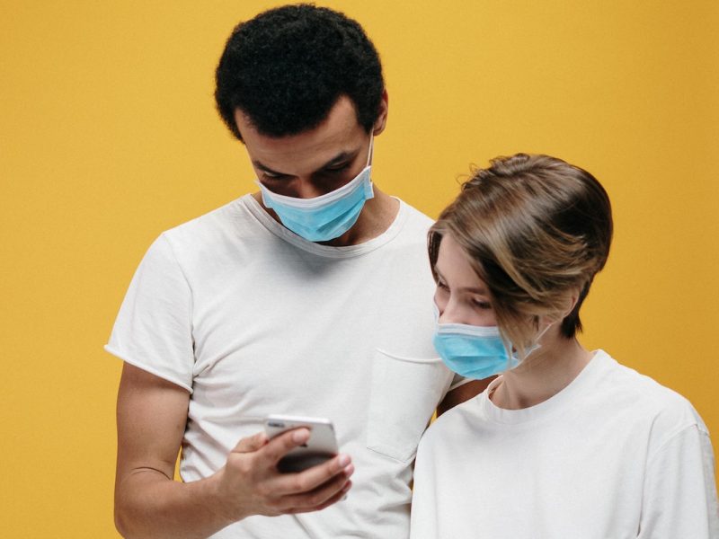 Zwei Personen mit Gesichtsmaske schauen auf ein Smartphone
