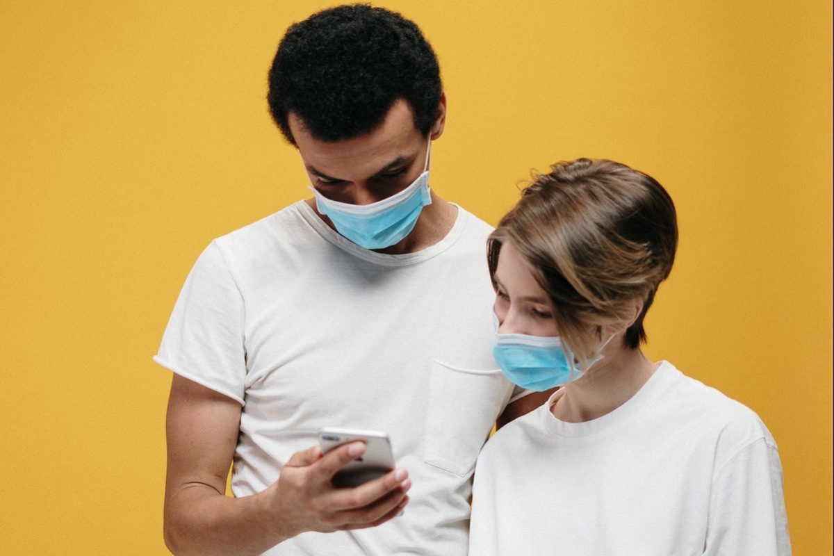 Zwei Personen mit Gesichtsmaske schauen auf ein Smartphone