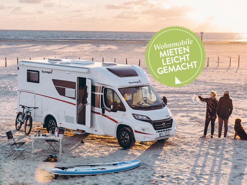 Älteres Paar steht neben Wohnmobil am Strand bei Sonnenuntergang.