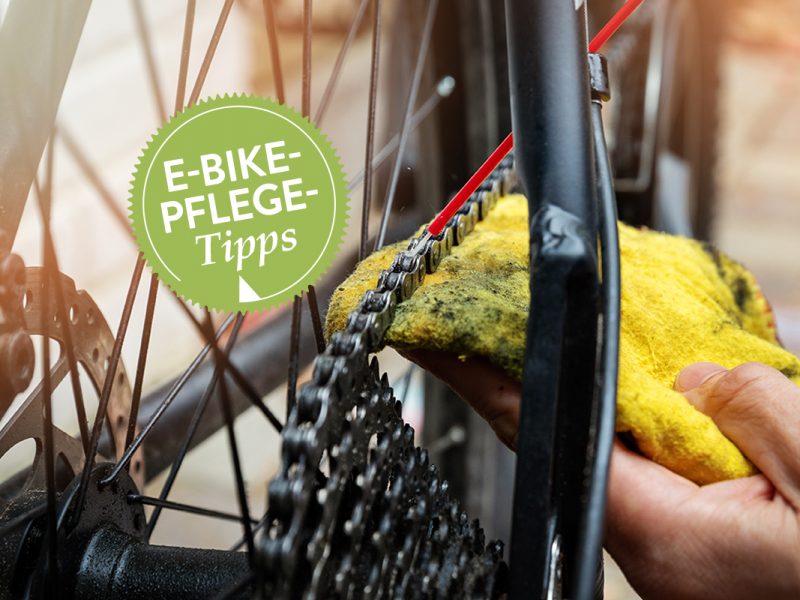 Eine Hand, die ein Tuch hält, putzt die Fahrradkette eines E-Bikes.