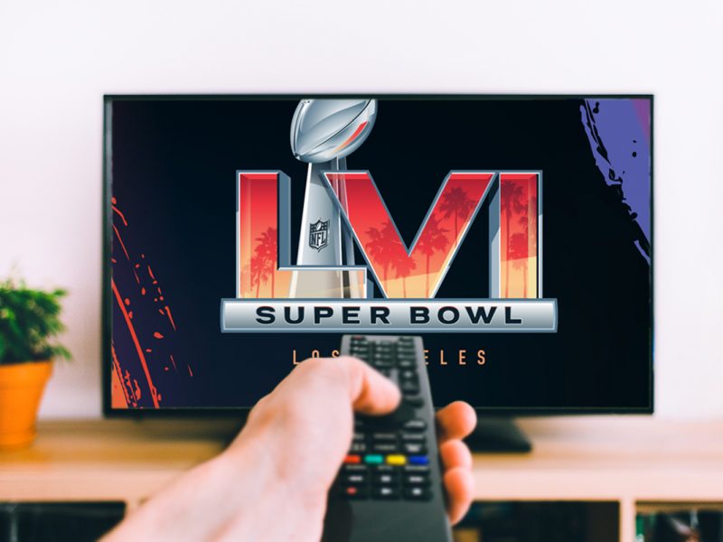 Hand hält Fernbedienung zu Fernseher, der Super-Bowl-Logo zeigt
