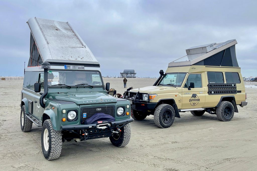 Ein Land Rover und Toyota Land Cruiser stehen mit aufgestellten Hochdächern am Strand.