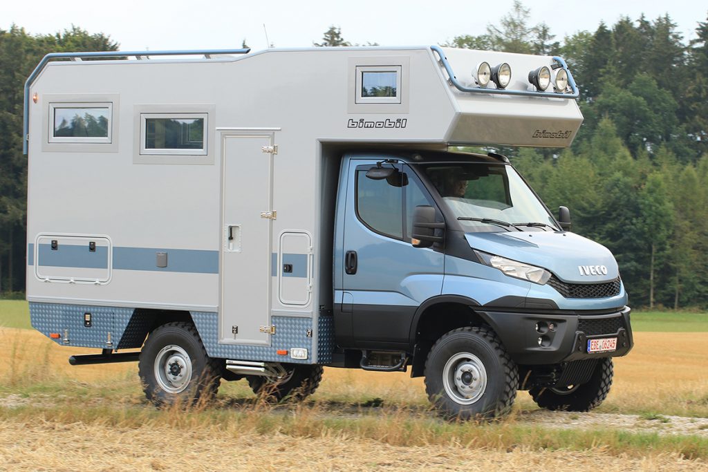 4x4-Transporter mit mit speziell angefertigter Kabine unterwegs auf einem Feldweg vor Waldlandschaft.