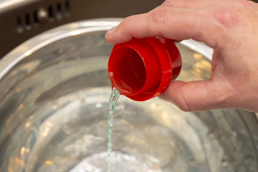Hand kippt Flüssigkeit mit roter Kappe in Wasser