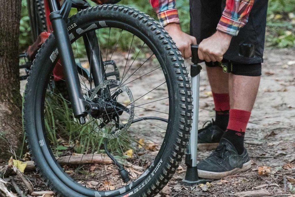 Mann pumpt im Wald einen platten Fahrradreifen mit einer Stand-Luftpumpe auf