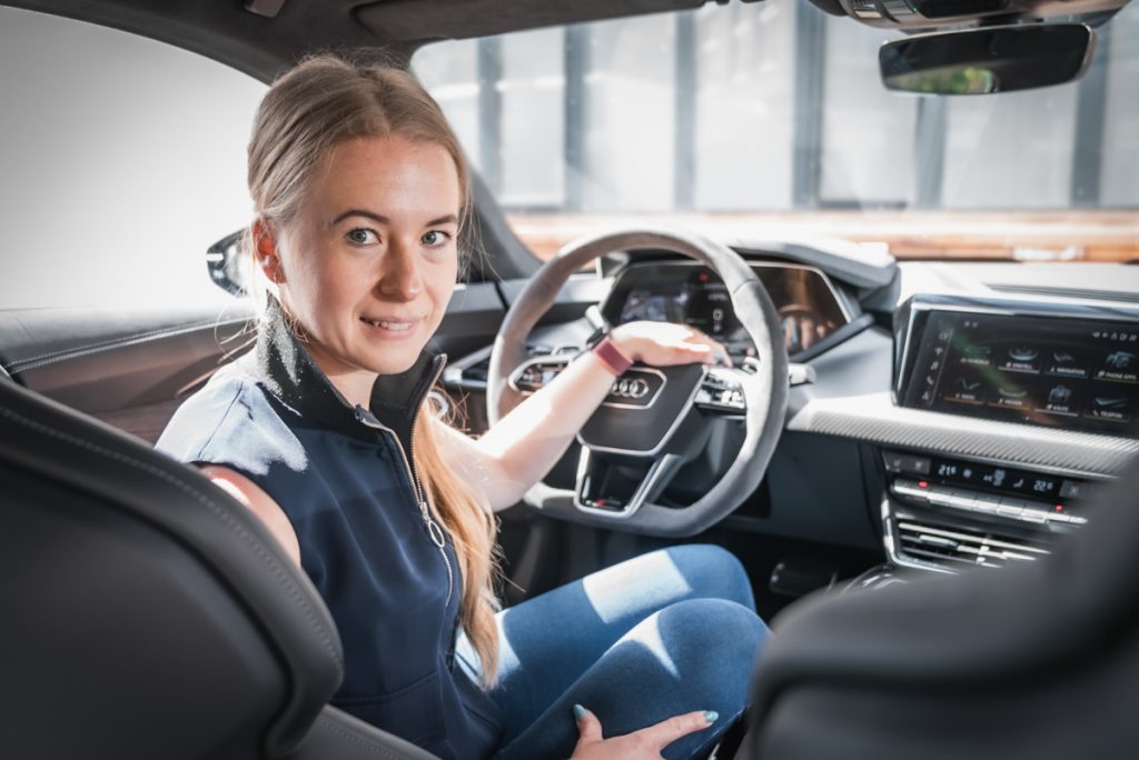 Frau am Steuer des Audi RS e-Tron GT im Test schaut lächelnd über die Schulter