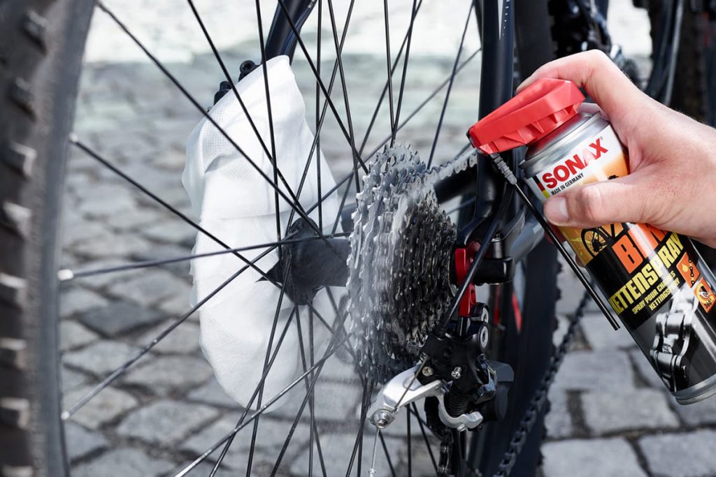 Kettenspray wird zum Reinigen einer Fahrradkette auf Ritzel und Kette an einem E-Bike aufgesprüht.