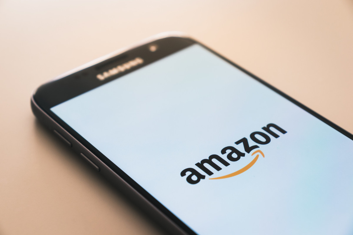 Schwarzes Smartphone liegt auf hellroter Fläche und zeigt amazon Logo