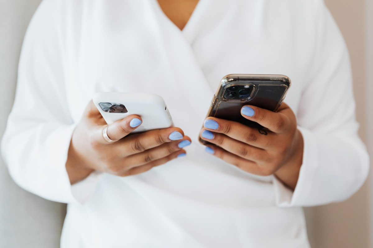 In weiß gekleidetes Person hält zwei iPhones vor ihrem Körper