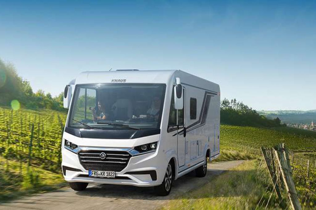 Wohnmobil fährt bei Sonnenschein und blauem Himmel durch Weinberge.