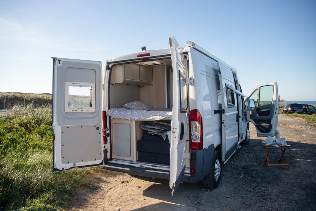 Ein Camper mit geöffneter Heckklappe auf einem Strandweg