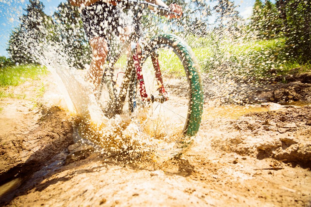 Ein E-Bike fährt mit viel Schwung durch eine große Pfütze, so dass das Wasser hoch spritzt.