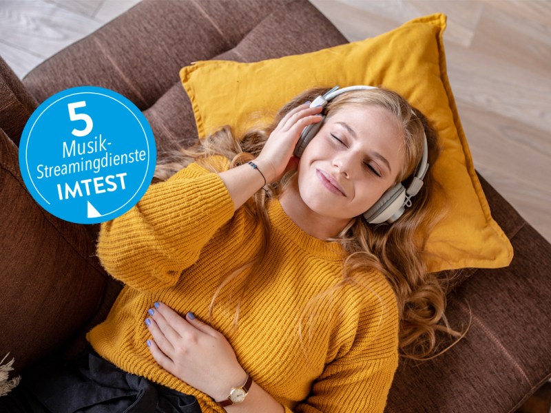 Mujer joven sonriente tumbada en el sofá con auriculares