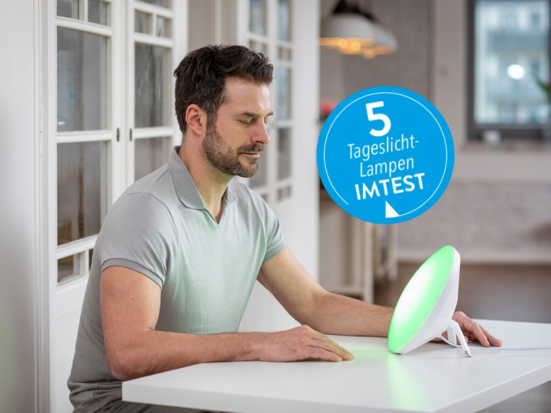 Junger Mann im Tshirt sitzt an weißem Tisch und lässt sich von runder Lampe anstrahlen