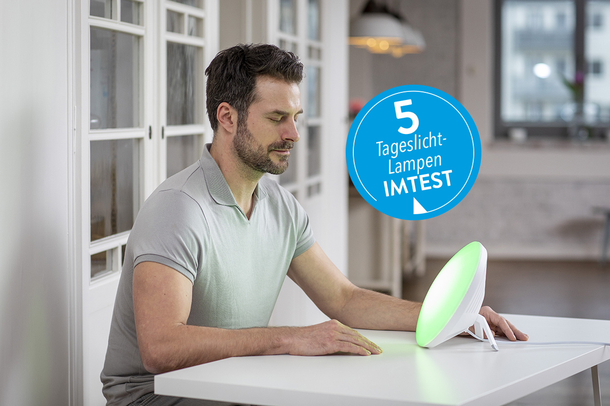 Junger Mann im Tshirt sitzt an weißem Tisch und lässt sich von runder Lampe anstrahlen