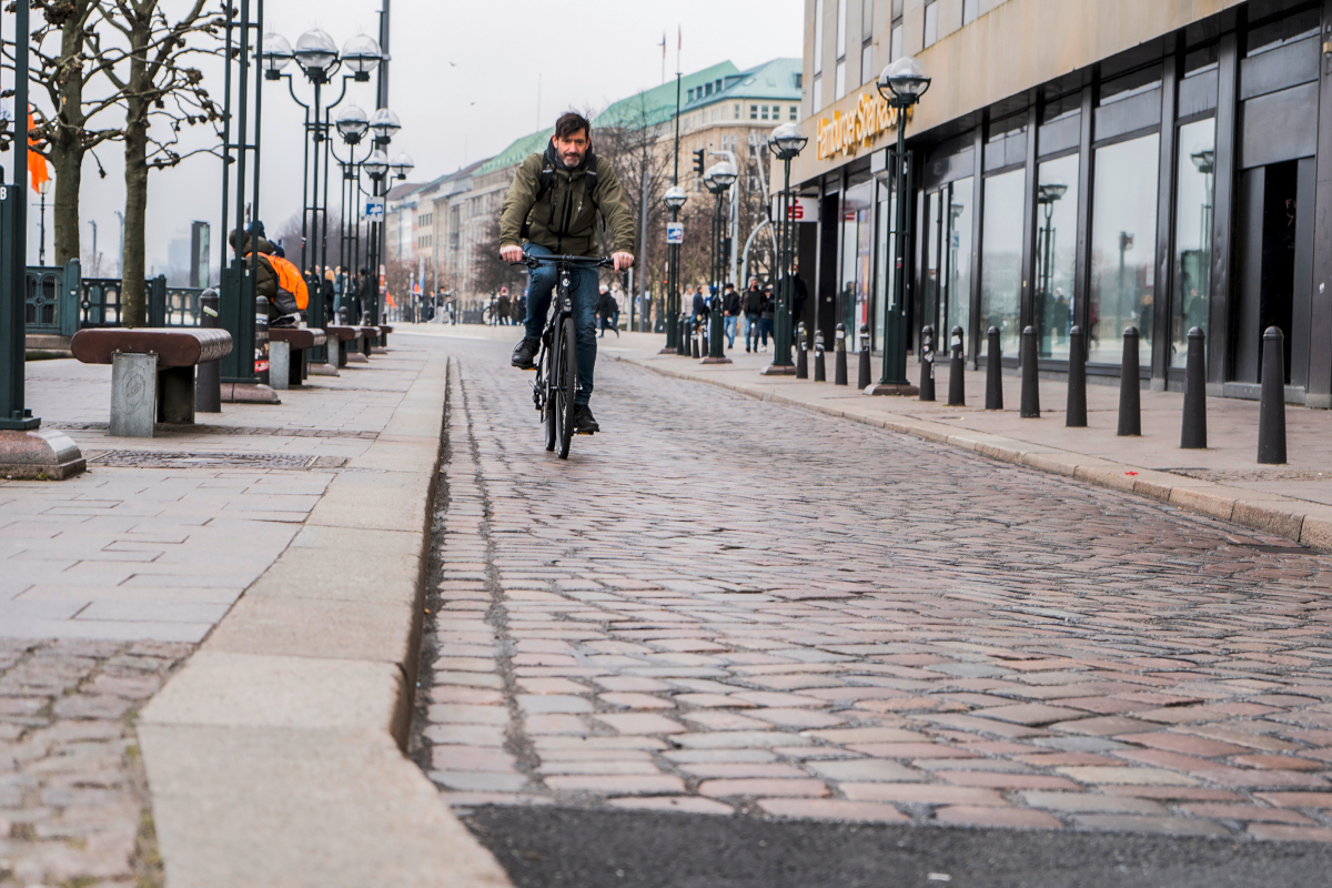 Mann fährt auf Urban-E-Bike auf Kopfsteinpflaster der Kamera entgegen