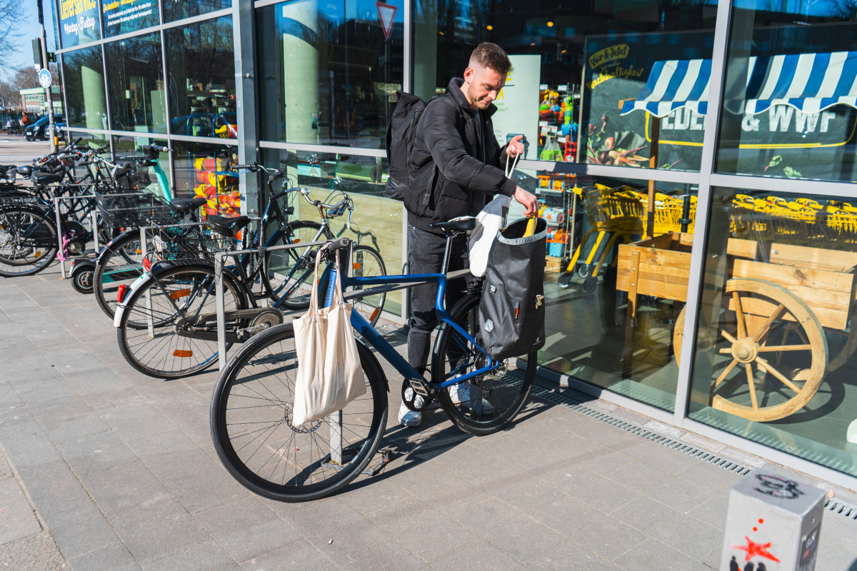 Junger Mann belädt blaues Urban-E-Bike mit Einkaufstaschen