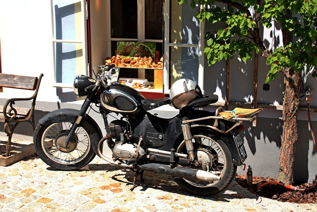 Älteres Motorrad steht im Sonnenschein vor einem Haus.