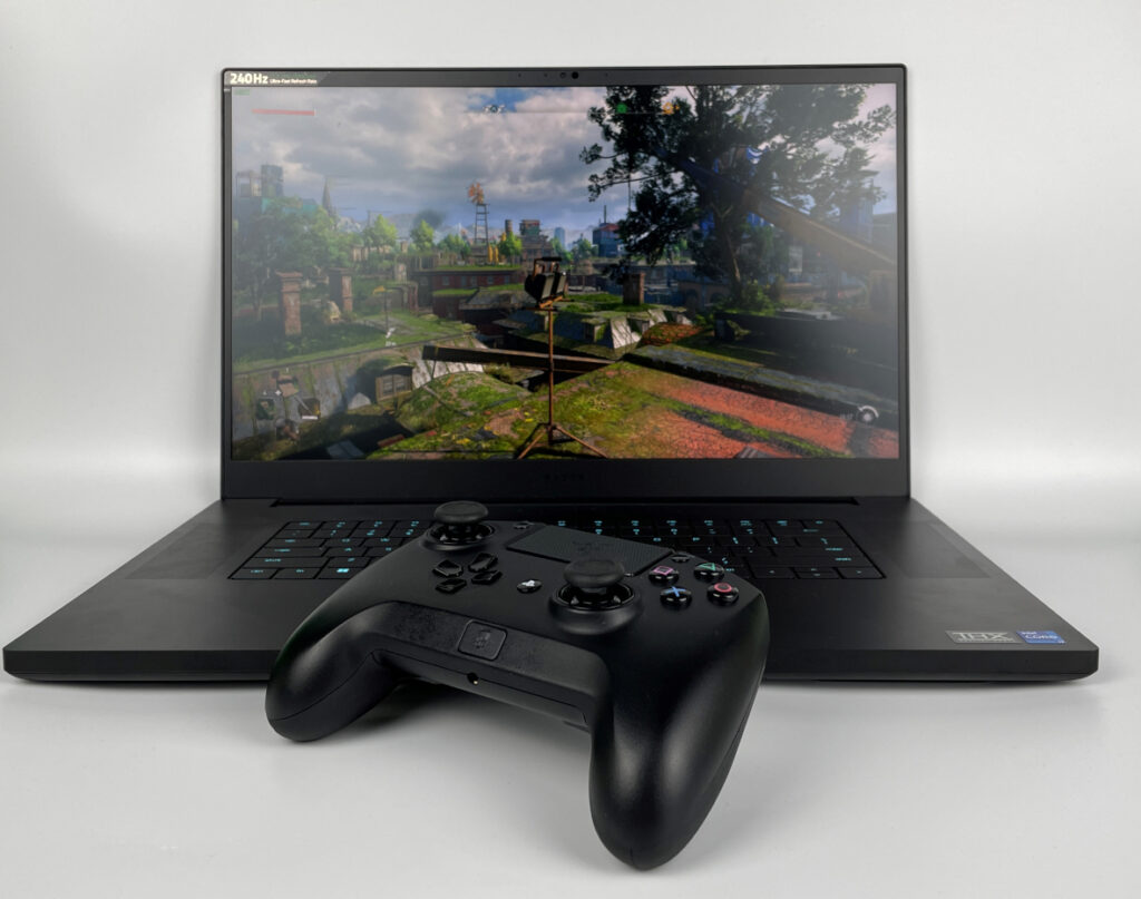 Aufgeklapptes schwarzes Razer Blade 17 Notebook zeigt Spielszene, mit Gamepad davor