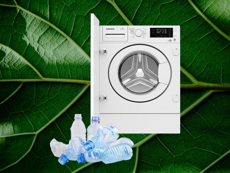 Weiße Grundig-Waschmaschine vor grünem Blatt-Hintergrund