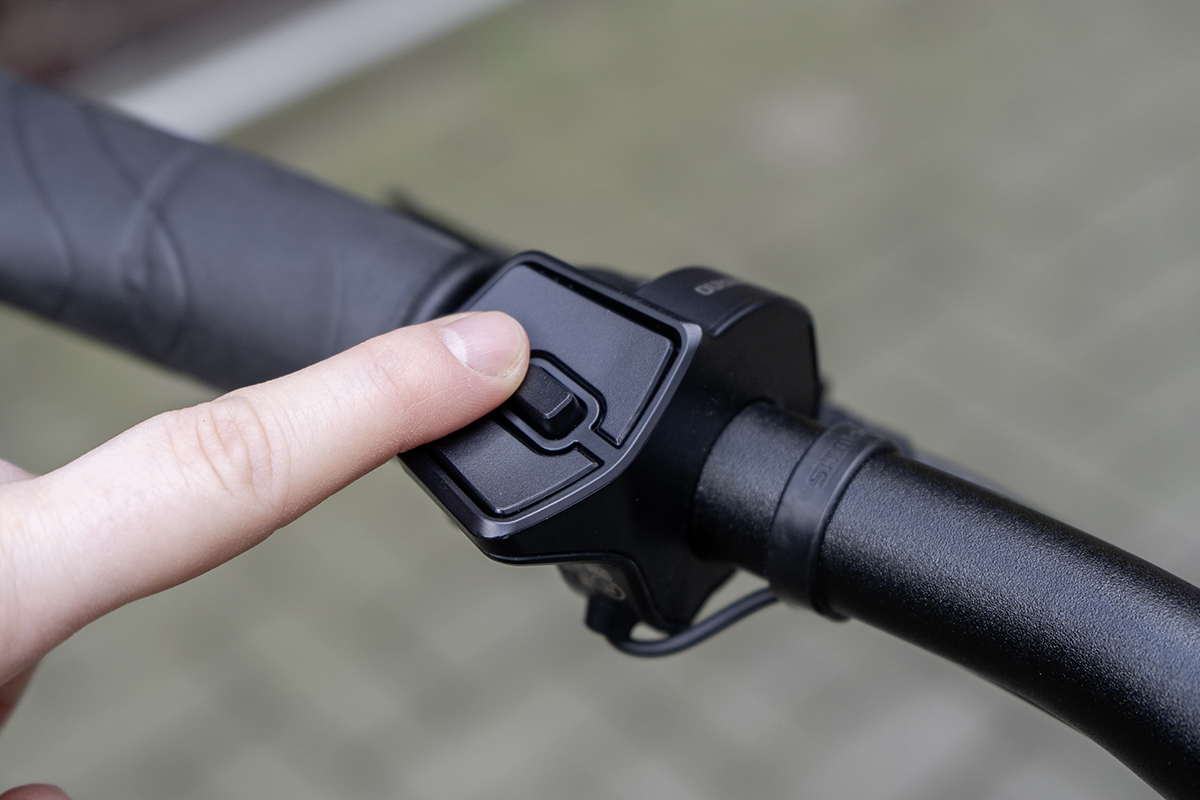 Finger zeigt auf Bedienung an schwarzem Lenker von E-Bike