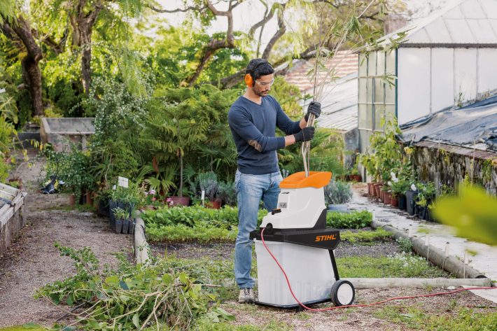 Mann häckselt Gartenabfälle in einem Elektrohäcksler im Garten