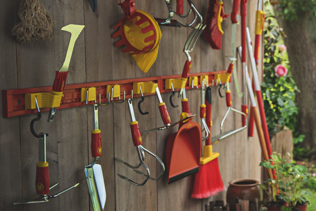 Unterschiedliche Gartenwerkzeuge hängen an einem Werkzeughalter, der an einer Schuppenwand angebracht ist.
