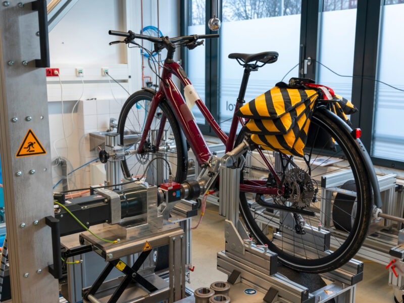 E-Bikes im Test hier rotes E-Bike auf Prüfstand mit Gewichten auf Gepäckträger