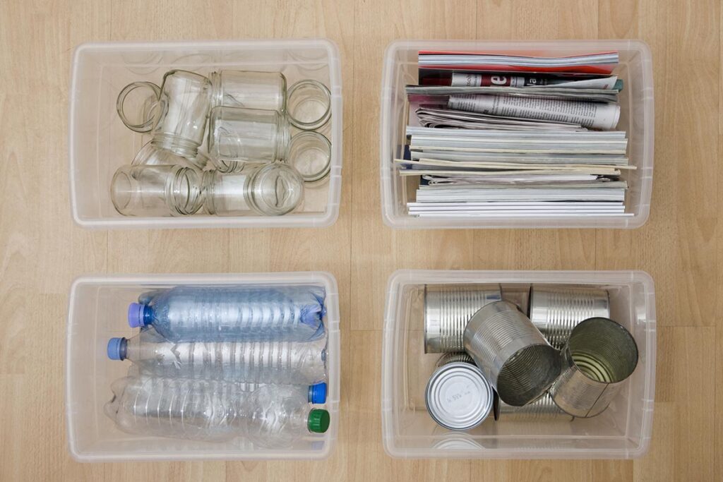 Vier durchsichtige Behälter von oben mit unterschiedlichen Wertstoffen wie Plastikflaschen und Papier