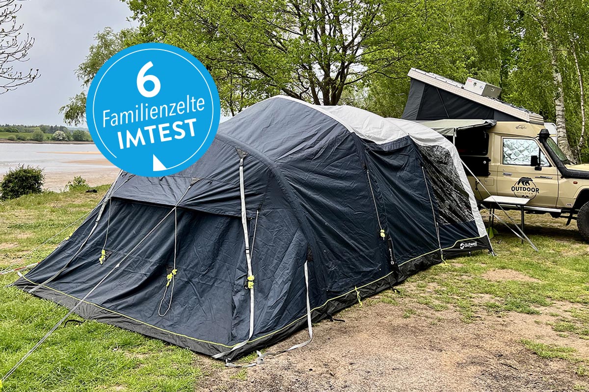 Dunkles großes aufgebautes Zelt auf Wiese vor Camper mit blauem Sticker "6 Familienzelte IMTEST"