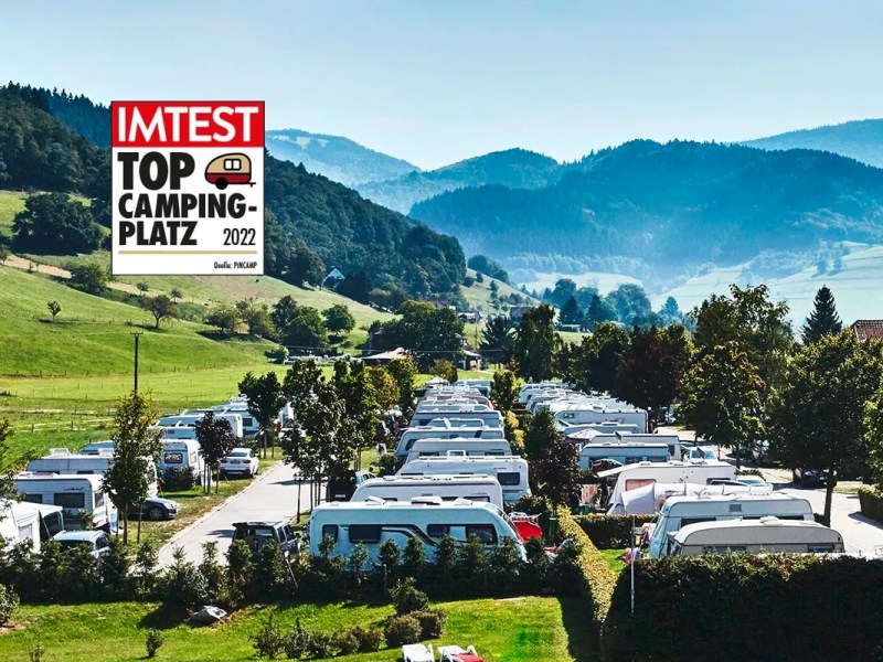 Grüner Campingplatz in den Bergen von schräg oben mit vielen Wohnwagen und IMTEST-Siegel links oben "Top Campingplatz 2022"