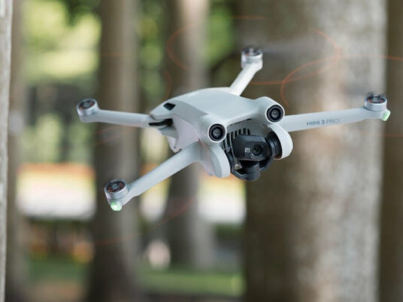 Die Drohne DJI Mini 3 Pro fliegt zwischen Bäumen.
