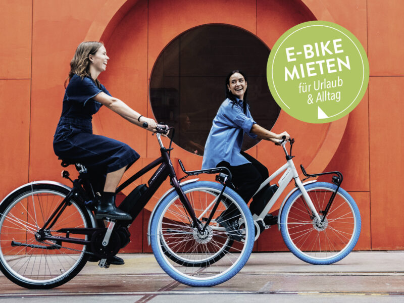 Zwei Frauen fahren auf einem Mietrad.
