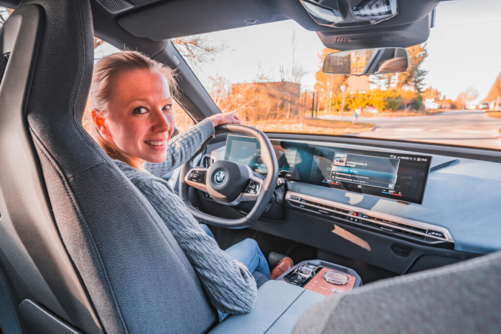 Lächelnde Frau sitzt am Steuer vom BMW iX und schaut über Schulter in Kamera