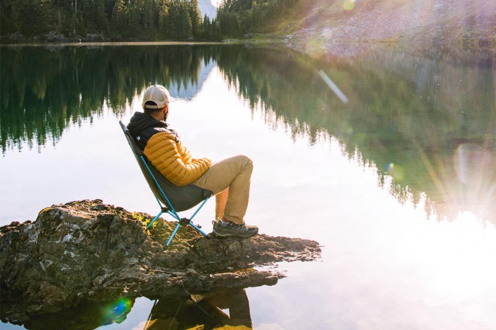 Person draußen an See auf Camping-Stuhl von der Seite