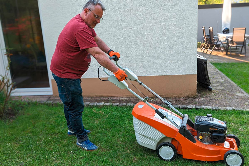 Eine Person steht auf der Wiese und mäht den Rasen.