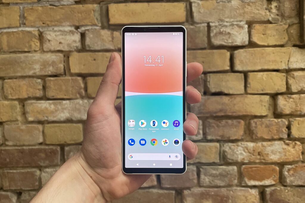 Sebuah tangan memegang Sony Xperia 10 IV di depan dinding bata.