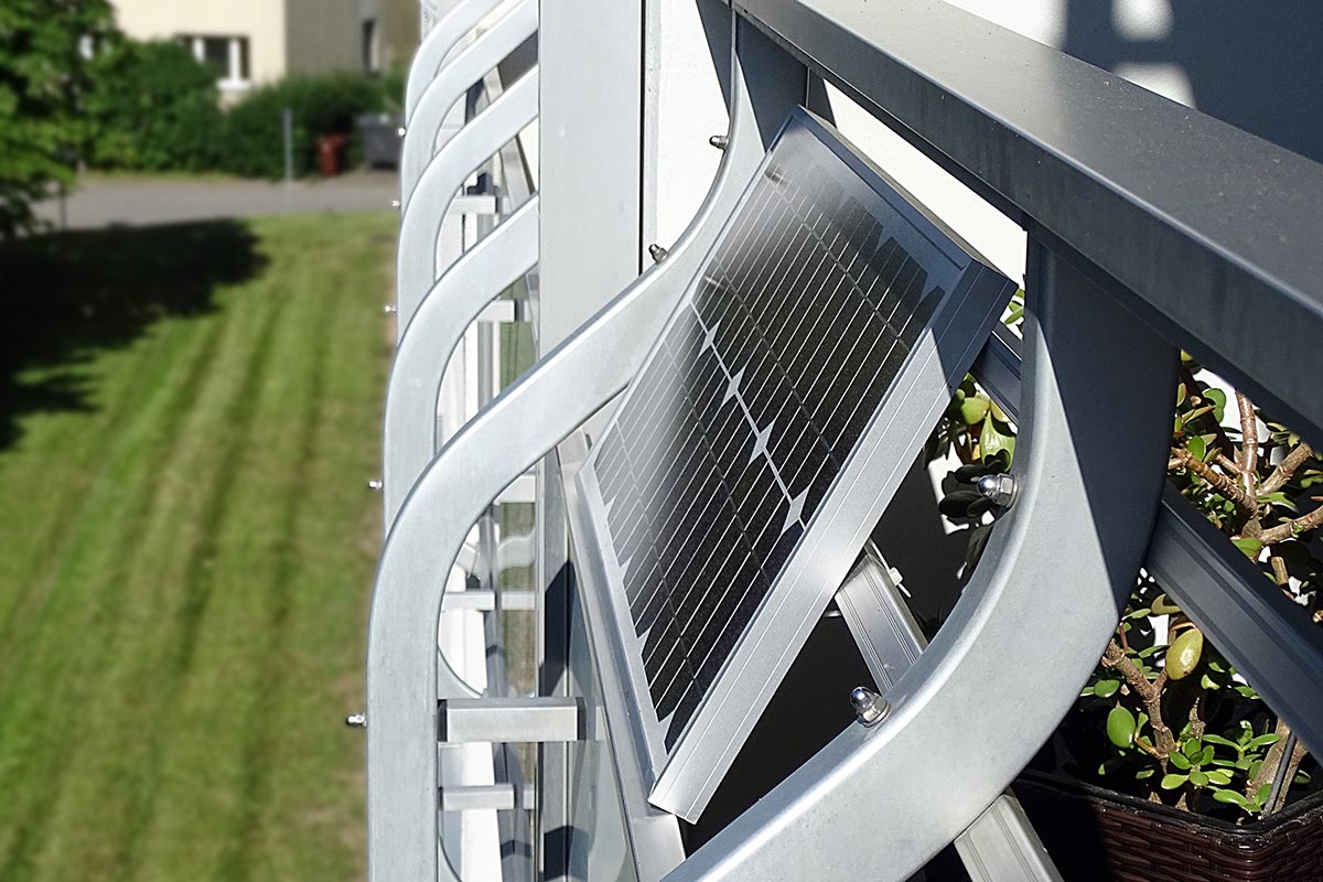 Solarmodul als Balkonkraftwerk am silbernen Balkongeländer von der Seite mit Blick auf Rasenfläche links