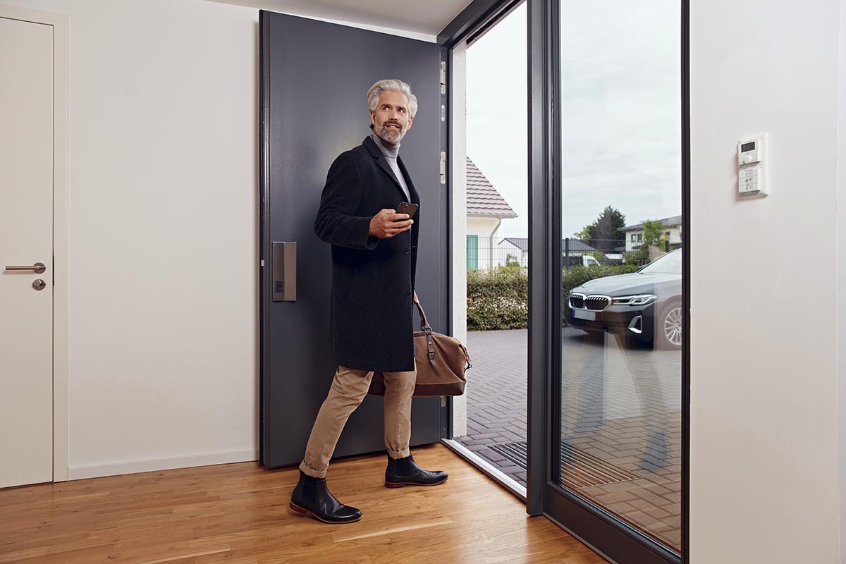 Ein Mann geht mit einem Smartphone in der Hand aus der Tür