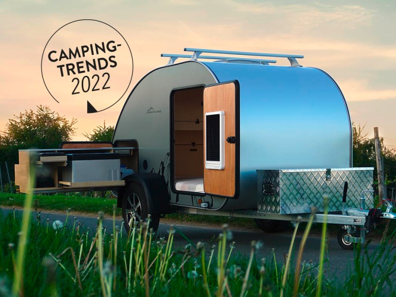 Kleiner silberner Wohnwagen vor Wiese bei Sonnenuntergang mit Schriftzug "Camping Trends 2022"