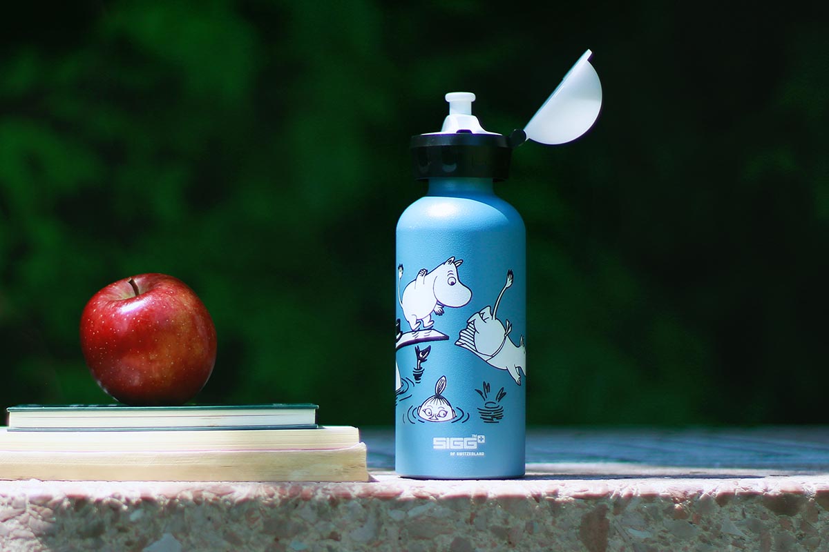 Eine Trinkflasche von SIGG neben einem Apfel und Schulbüchern.