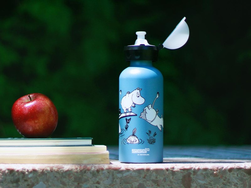Eine Trinkflasche von SIGG neben einem Apfel und Schulbüchern.
